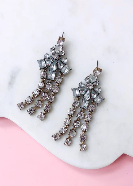 Dangling crystal chandelier earrings with clear and gray gemstones on white marble